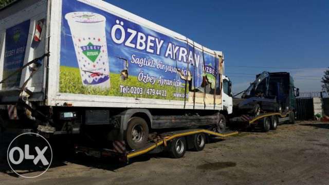 Laweta przewozi uszkodzony samochód osobowy; na pierwszym planie ciężarówka z reklamą napoju Ayran.