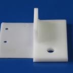 Biały, precyzyjnie obrobiony element z tworzywa sztucznego o kształcie kątownika z otworami, na jednolitym niebieskim tle.