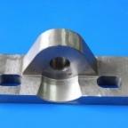 Metalowy element obrobiony z widocznymi śladami frezowania, z otworem centralnym i dwoma prostokątnymi wycięciami, na jednolitym niebieskim tle.