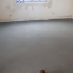 Świeżo wylana, gładka posadzka w surowym wnętrzu z widocznym żółtym urządzeniem do jej przygotowania.