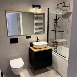 Remokompleks Michał Motyl - Nowoczesna łazienka w szarościach: wisząca toaleta, czarna szafka z umywalką, lustro w drewnianej ramie, kabina prysznicowa z czarną armaturą. Minimalistyczny design.