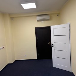 Remokompleks Michał Motyl - Pomalowane na jasnożółto wnętrze z ciemną podłogą, białą, nowoczesną ościeżnicą i klimatyzacją na ścianie. Widoczne gniazdka i włączniki.