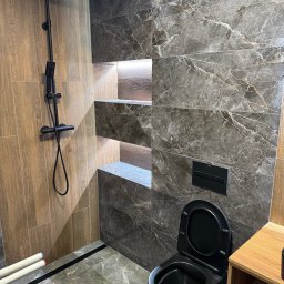 Remokompleks Michał Motyl - Nowoczesna łazienka w Poznaniu z czarną armaturą i płytkami imitującymi marmur. Podświetlane półki wnękowe dodają elegancji.