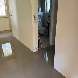 Remokompleks Michał Motyl - Wnętrze w trakcie prac wykończeniowych: wylana posadzka samopoziomująca, ściany przygotowane pod malowanie, widoczna łazienka z toaletą.