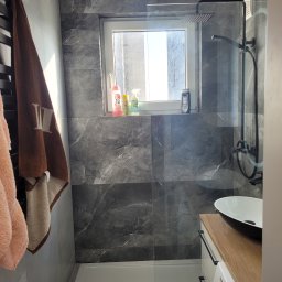 Remokompleks Michał Motyl - Nowoczesna łazienka z szarymi płytkami imitującymi marmur, kabiną prysznicową typu walk-in i umywalką nablatową. Okno z widokiem na budynek.
