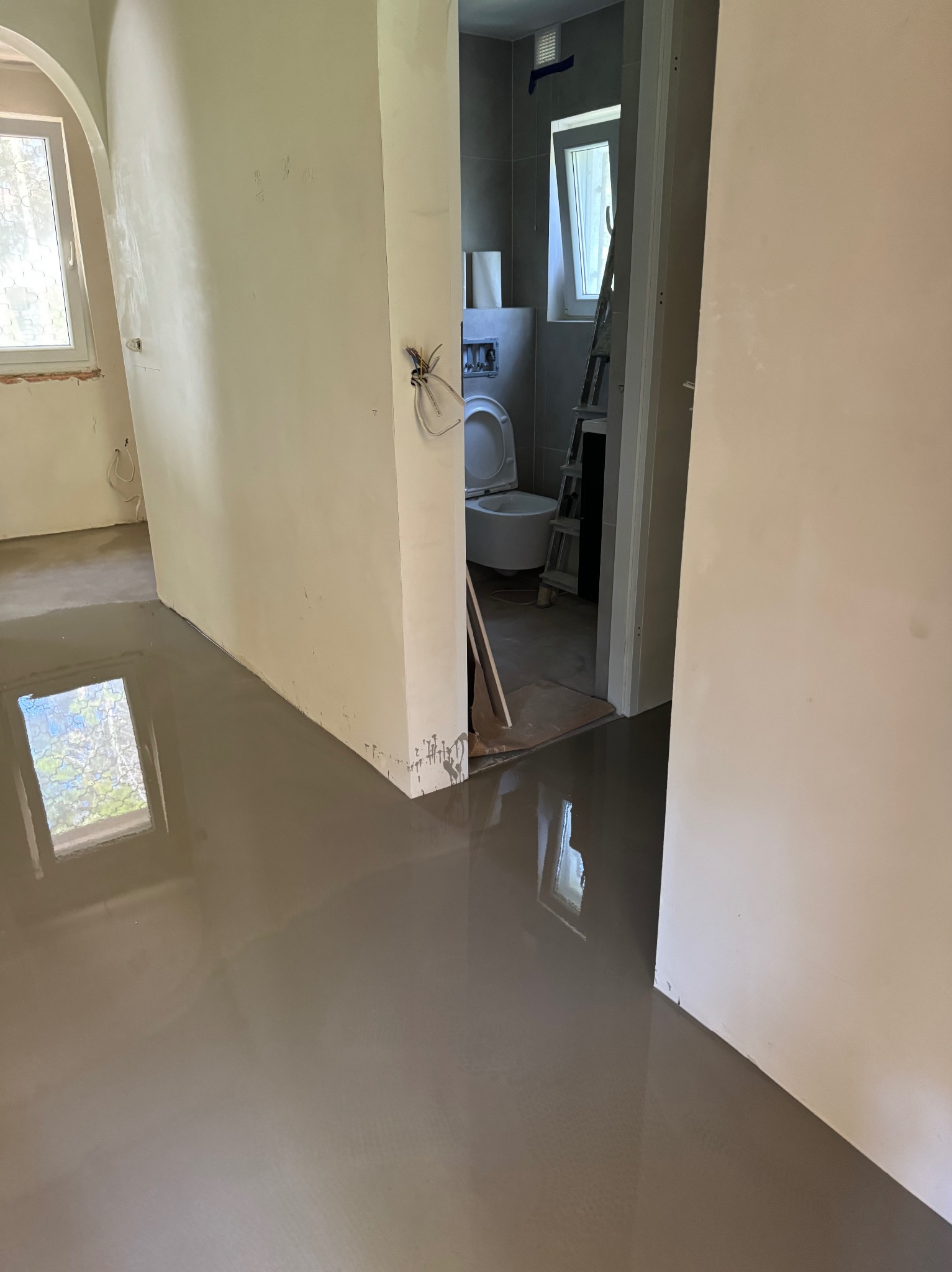 Wnętrze w trakcie prac wykończeniowych: wylana posadzka samopoziomująca, ściany przygotowane pod malowanie, widoczna łazienka z toaletą.