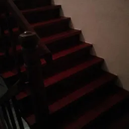 Ciemne, drewniane schody z poręczą w klatce schodowej, oświetlone z góry, widok z dołu.