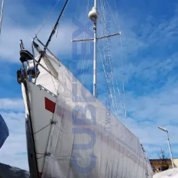 Jacht zabezpieczony plandeką na zimę, widoczny maszt i niebieskie niebo w tle.