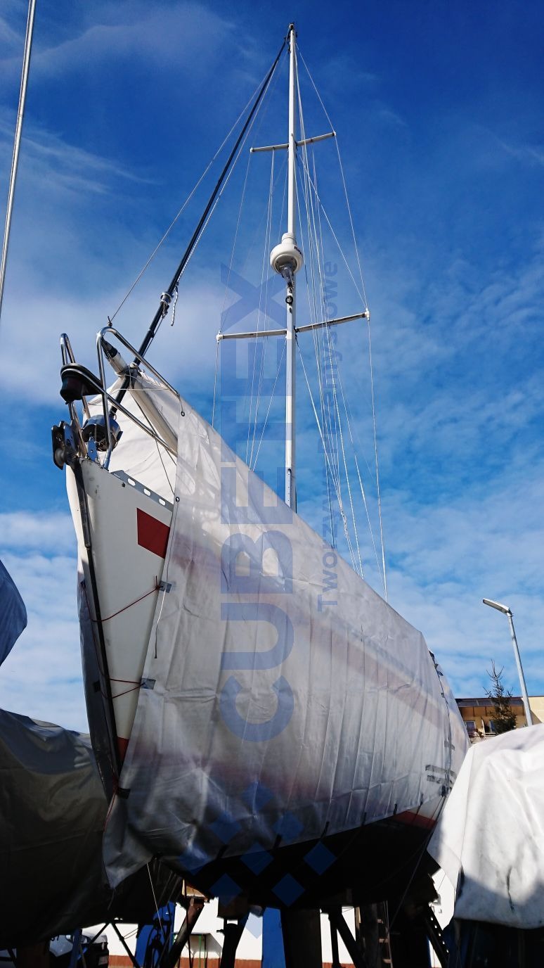 Jacht zabezpieczony plandeką na zimę, widoczny maszt i niebieskie niebo w tle.