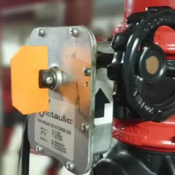 Czerwony zawór systemu przeciwpożarowego Victaulic z czarnym pokrętłem i pomarańczową osłoną zabezpieczającą.