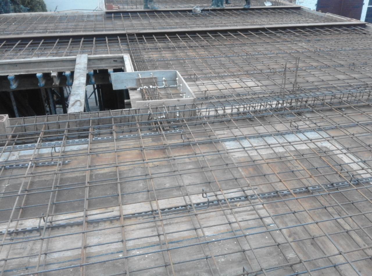 Zbrojenie stropu na budowie z widocznymi otworami i wystającymi prętami, częściowo zalane betonem.
