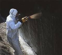 Pracownik w kombinezonie ochronnym rozpyla farbę z pistoletu natryskowego na ciemną powierzchnię. Widoczne ślady świeżo nałożonej farby.