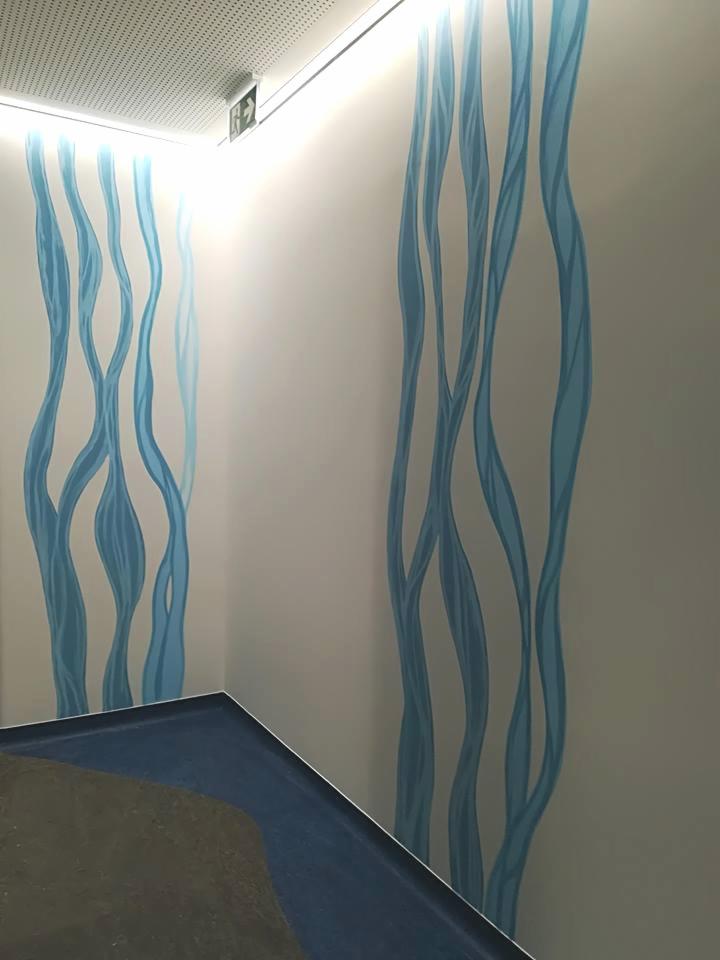 Dekoracyjna ściana z motywem abstrakcyjnych, pionowych, niebieskich linii przypominających rzeki, widoczny fragment schodów w dolnej części kadru.
