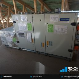 PRO-CON SERWIS Klimatyzacja Wentylacja Rekuperacja - Centrala wentylacyjna Komfovent Verso, zamontowana na poddaszu, widoczne drewniane elementy konstrukcji dachu, dokumentacja techniczna przyklejona do obudowy urządzenia.