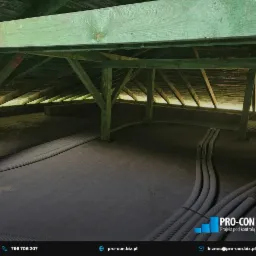 Instalacja przewodów wentylacyjnych w przestrzeni poddasza z drewnianą konstrukcją nośną, widoczne rury karbowane prowadzone po podłodze.