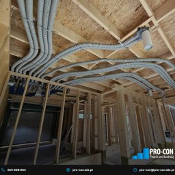 PRO-CON SERWIS Klimatyzacja Wentylacja Rekuperacja - Szare, elastyczne rury wentylacyjne zamontowane pod drewnianym stropem w surowym budynku. Widoczne elementy instalacji i konstrukcja szkieletowa.