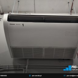 PRO-CON SERWIS Klimatyzacja Wentylacja Rekuperacja - Zamontowana pod sufitem klimatyzacja Panasonic z widocznymi filtrami i numerem '1', instalacja elektryczna w korytku. Szare ściany i sufit. Ujęcie z dołu.