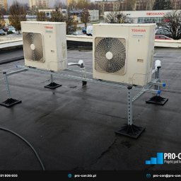 PRO-CON SERWIS Klimatyzacja Wentylacja Rekuperacja - Dwa klimatyzatory Toshiba Digital Inverter na dachu budynku, zamontowane na metalowej konstrukcji wsporczej. Widok na Rossmann w tle.