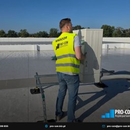 PRO-CON SERWIS Klimatyzacja Wentylacja Rekuperacja - Pracownik w kamizelce odblaskowej montuje klimatyzator na dachu budynku. Widoczne elementy instalacji i narzędzia. Jasne niebo w tle.