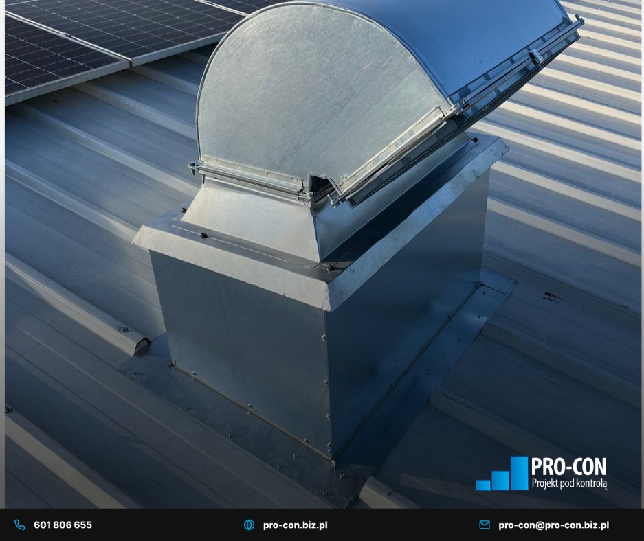 Metalowa nasada wentylacyjna na dachu z blachy trapezowej, widoczne panele słoneczne w tle. Ujęcie z góry, oświetlenie dzienne.