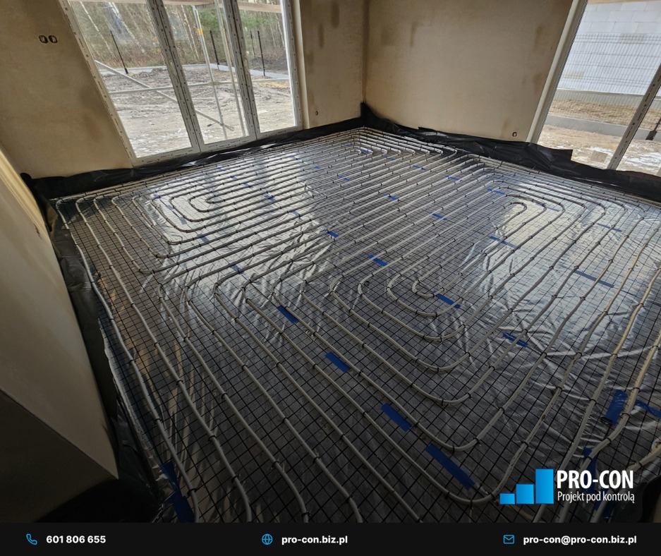 Ułożone rury ogrzewania podłogowego na czarnej folii, przymocowane do siatki w surowym wnętrzu z oknami. Widoczny logotyp firmy w prawym dolnym rogu.