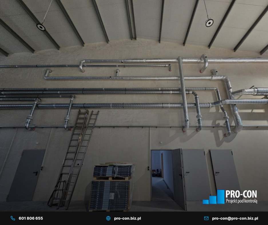 Instalacja wentylacyjna z rurami w izolacji, drabina oparta o ścianę, paleta z materiałami. Widok na sufit z elementami instalacji. Hala w stanie surowym.