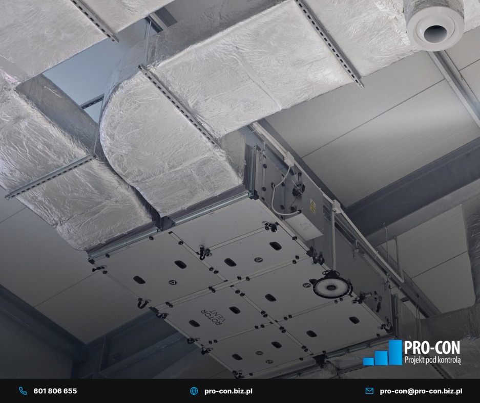 Srebrne, izolowane kanały wentylacyjne pod sufitem, z widocznym systemem rozprowadzającym powietrze. Elementy montażowe i oświetlenie w tle.