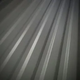 Szare arkusze profilowanej blachy z widocznym połyskiem, ułożone jedna na drugiej w ciemnym pomieszczeniu.