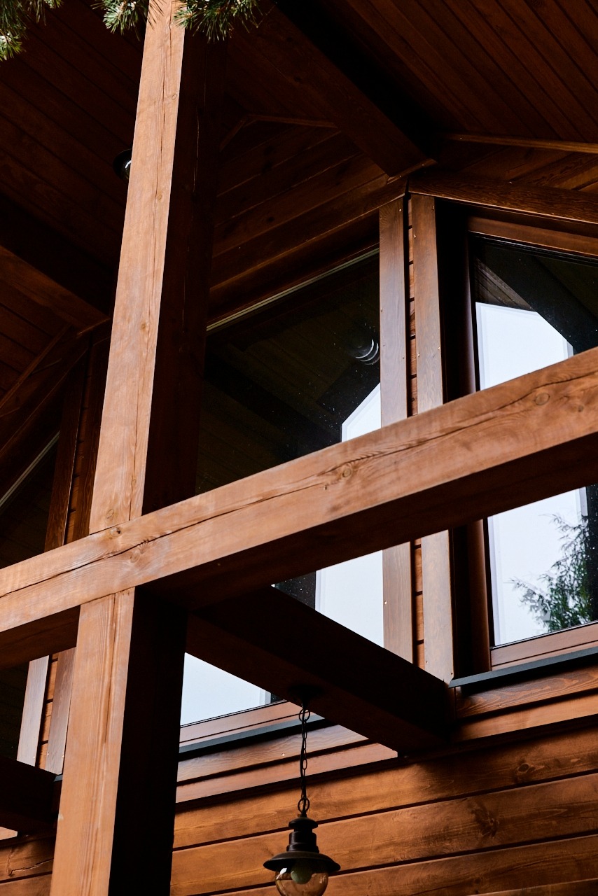 Drewniana elewacja domu z oknami, widok z dołu. Elementy konstrukcyjne i dekoracyjne z drewna, lampa wisząca. Detal wykończenia zewnętrznego budynku.