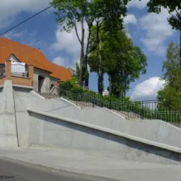 Klasztor Benedyktynek w Sierpcu po renowacji, widoczny z poziomu ulicy, z nowym, betonowym murem oporowym i schodami prowadzącymi do wejścia.