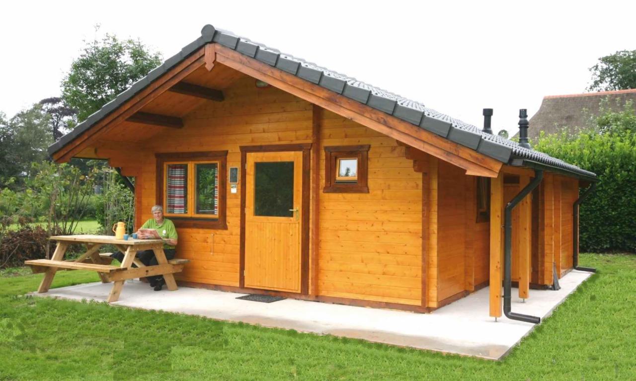 Drewniany dom z bali z czarną dachówką w Opolu, z zewnątrz widoczny stół piknikowy z siedzącą osobą i dzbankiem.