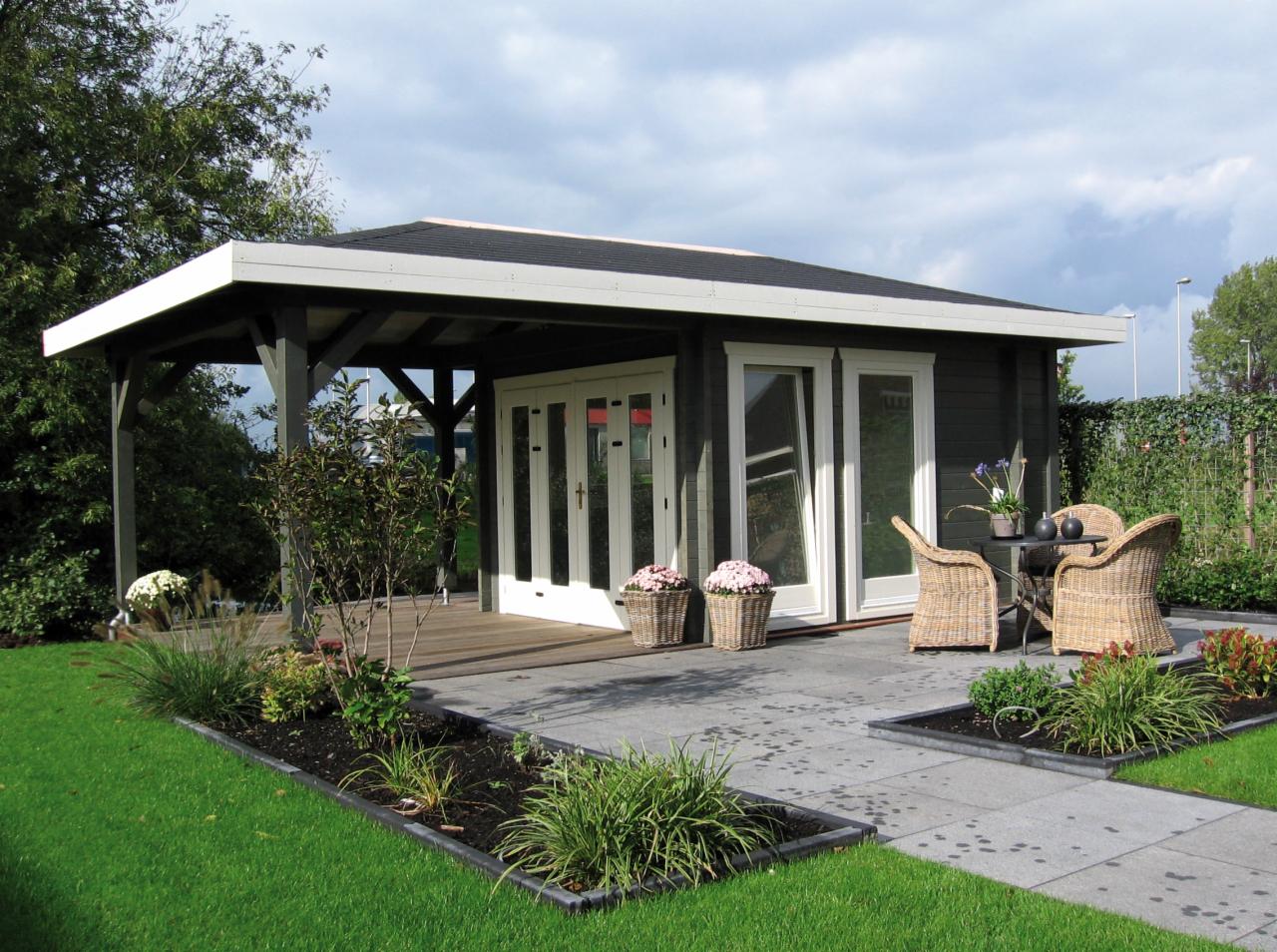 Drewniany domek letniskowy z zadaszoną werandą, otoczony wypielęgnowanym ogrodem z rabatami i ścieżką z płyt.