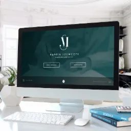 Monitor wyświetla stronę internetową kancelarii adwokackiej Marcina Szewczyka, z logo i przyciskami do działów Prawo Rodzinne i Prawo Karne. Na biurku obok klawiatura, mysz, telefon na książkach...