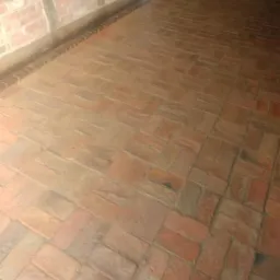 Podłoga z cegły klinkierowej ułożona w jodełkę w pomieszczeniu z murem pruskim, widoczny fragment ściany z cegły i drewnianej konstrukcji oraz biała lod&oacute;wka w tle.