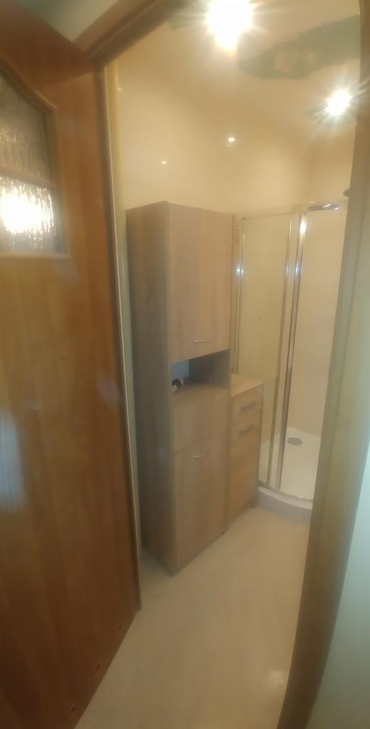 Jasna łazienka po renowacji w Tarzymiechy Drugie, z drewnianą szafką łazienkową i kabiną prysznicową z przezroczystego szkła.