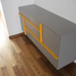 Szara szafka wisząca z ż&oacute;łtymi uchwytami na tle drewnianej podłogi.