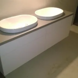 Nowoczesna łazienka z dwoma owalnymi, białymi umywalkami nablatowymi na białej szafce z szarym blatem, widok z boku.