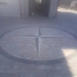 Ułożona kostka brukowa z dekoracyjnym motywem kompasu na podjeździe przed garażem.