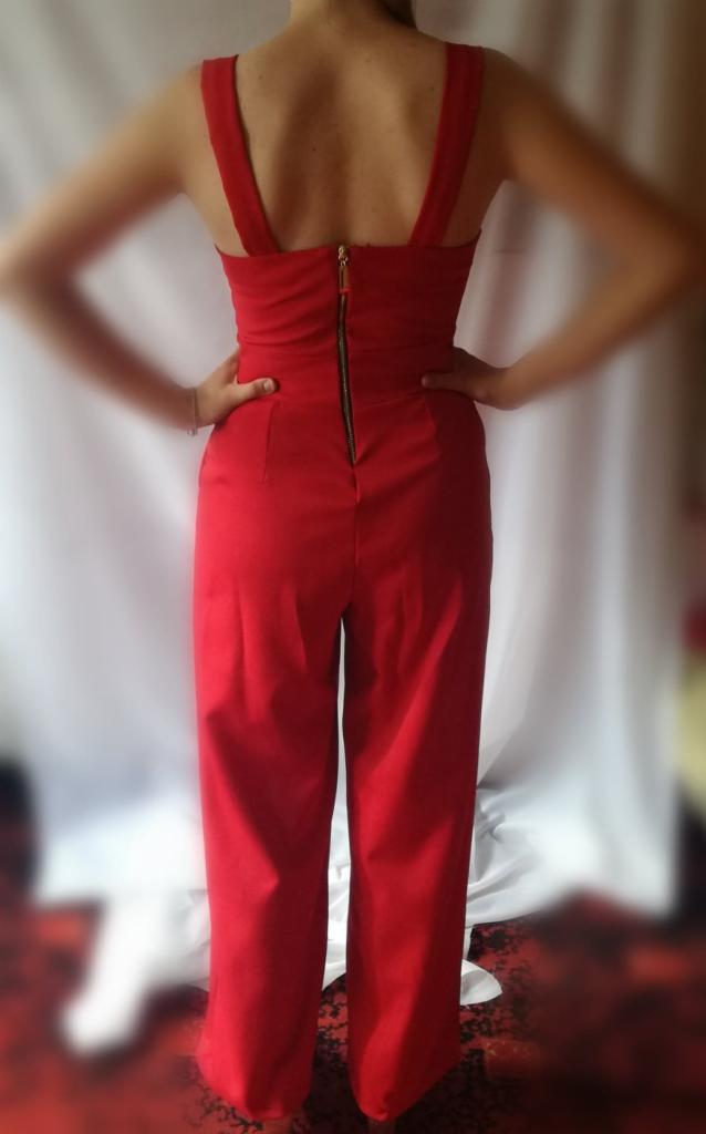 Czerwony damski kombinezon z widocznym zamkiem błyskawicznym na plecach, szerokie nogawki, osoba pozuje tyłem na tle białej tkaniny.