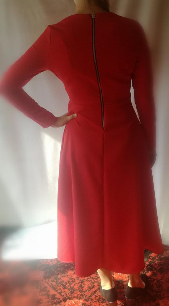 Czerwona, dopasowana sukienka z długim rękawem i zamkiem błyskawicznym z tyłu, widok od tyłu, dłoń na biodrze.