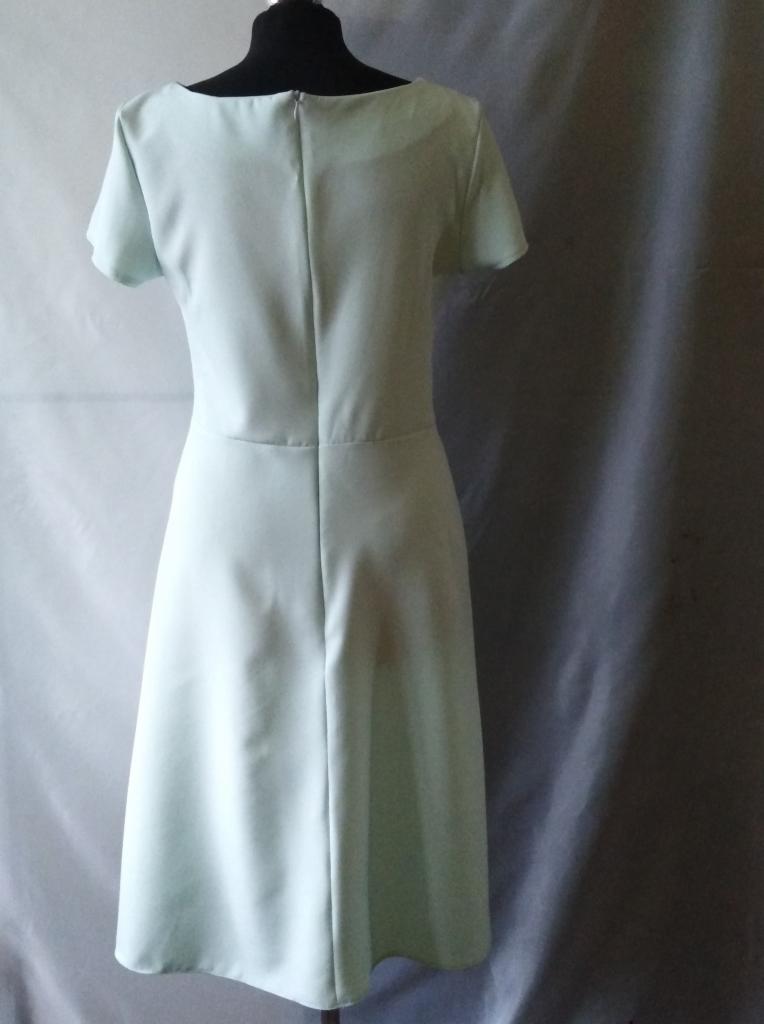 Jasnozielona, prosta sukienka z krótkim rękawem, widok z tyłu, na manekinie, z widocznym zamkiem błyskawicznym na plecach i delikatnym drapowaniem tła.