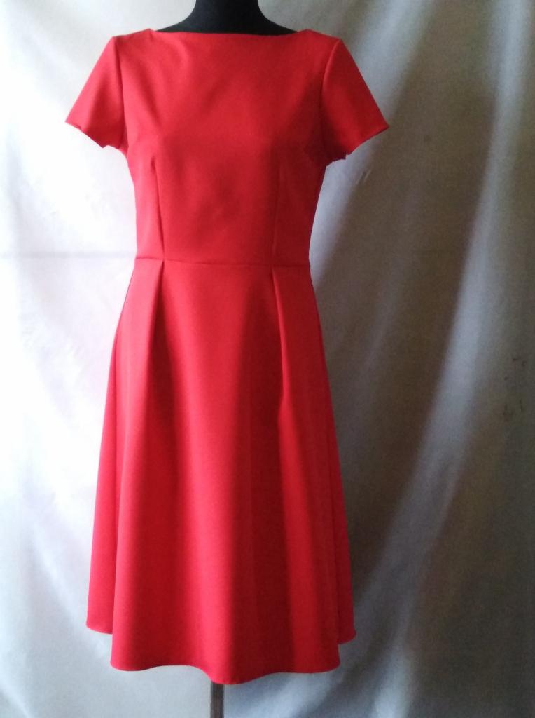 Czerwona, dopasowana sukienka z krótkim rękawem i plisowanym dołem, prezentowana na manekinie na tle jasnej tkaniny.