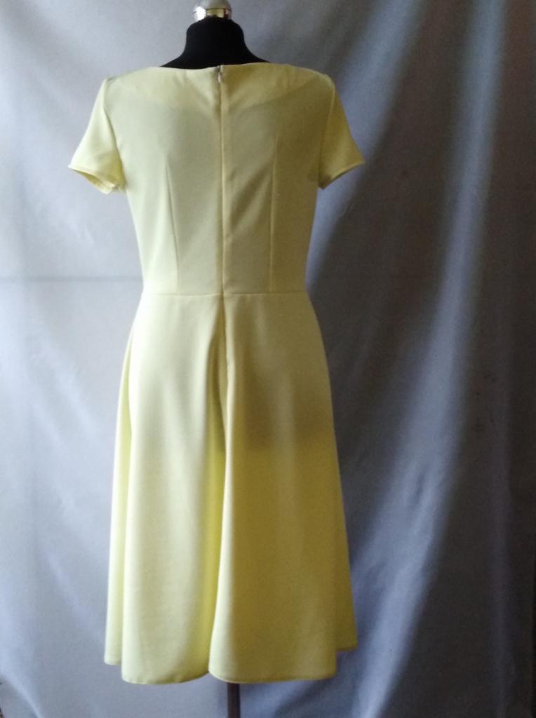 Jasnożółta, trapezowa sukienka damska z krótkim rękawem, widok z tyłu, na manekinie, z delikatnym zapięciem na zamek błyskawiczny.