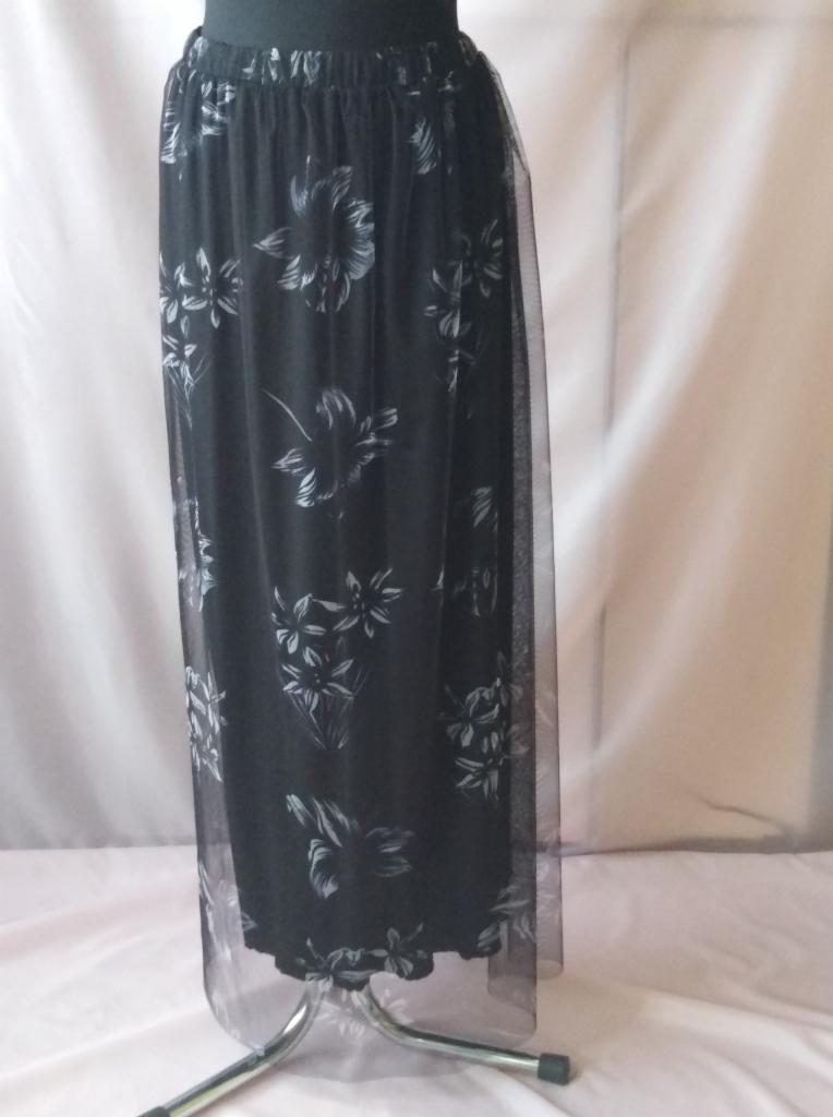 Czarna, długa spódnica z tiulu z białym kwiatowym wzorem, prezentowana na manekinie z metalową podstawą na tle białej tkaniny.