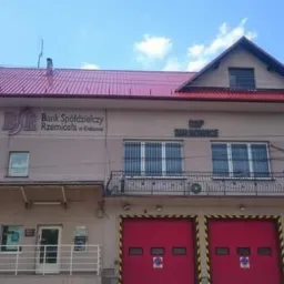Budynek z czerwonym dachem, częściowo zajmowany przez Bank Spółdzielczy Rzemiosła w Krakowie i OSP Surkowice, z czerwonymi bramami garażowymi.