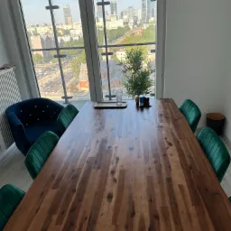 Sala konferencyjna z dużym drewnianym stołem, zielonymi krzesłami i widokiem na panoramę miasta przez okno.