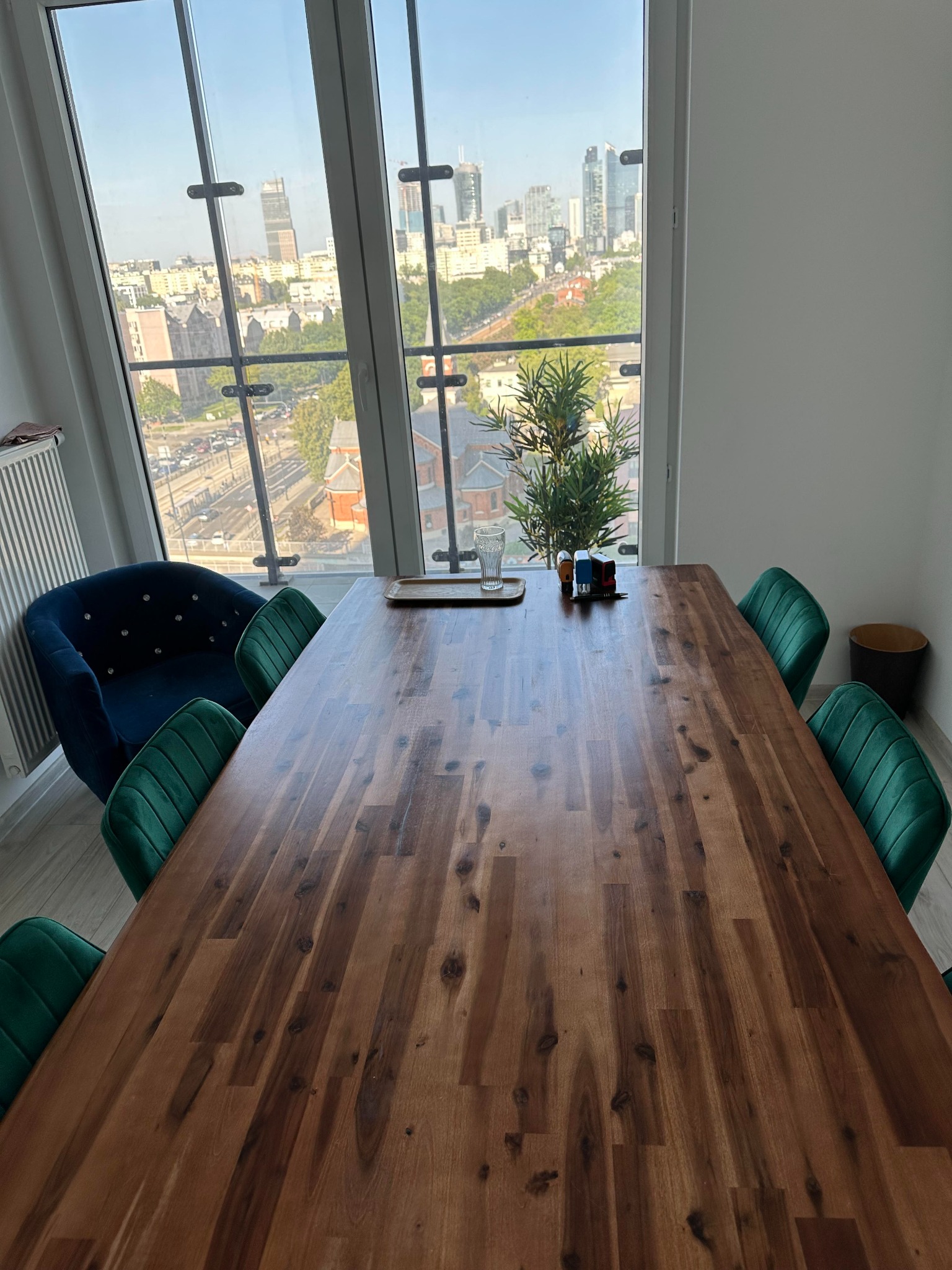 Sala konferencyjna z dużym drewnianym stołem, zielonymi krzesłami i widokiem na panoramę miasta przez okno.