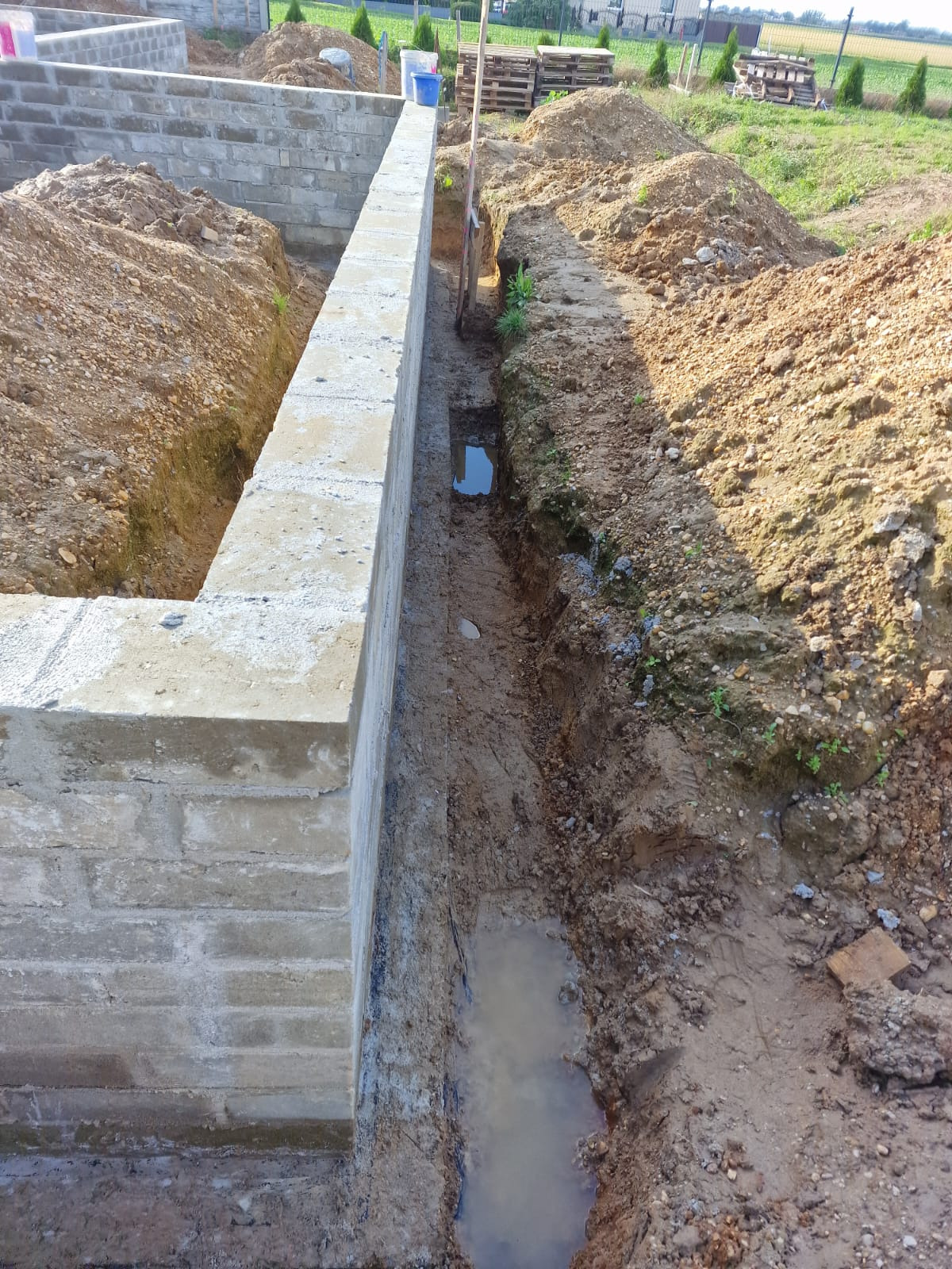 Wykop pod fundamenty domu z bloczków betonowych, częściowo zalany wodą, widoczne przygotowane podłoże i elementy szalunku.