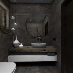 Nowoczesna łazienka z szarą kamienną ścianą, okrągłym lustrem, drewnianym blatem z umywalką, dekoracyjnymi lampami wiszącymi i białymi akcesoriami.