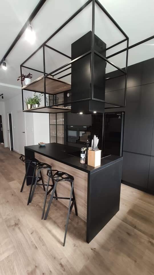 Nowoczesna kuchnia z czarną wyspą i metalową konstrukcją nad nią, uzupełniona drewnianymi akcentami i minimalistycznym oświetleniem.